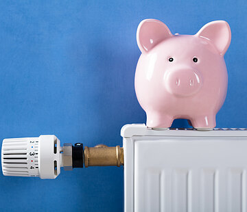 Close-up Of Piggy Bank On Heating Radiator Against Blue Background